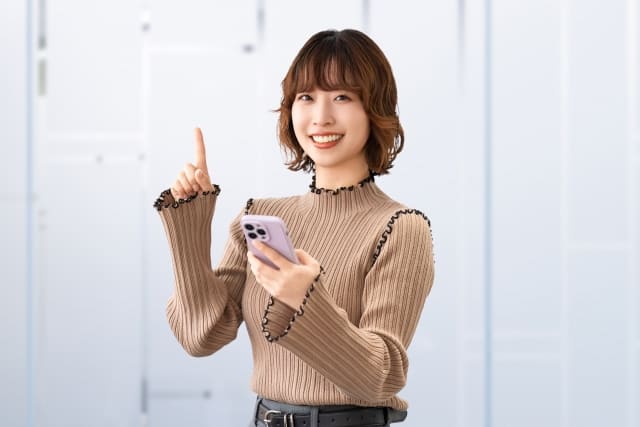 スマホを持ちながら人差し指を立てる女性